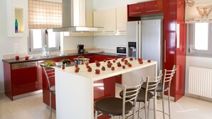 A modern kitchen with red cabinetry, a central island with chairs, stainless steel appliances, and a window with a butterfly curtain.