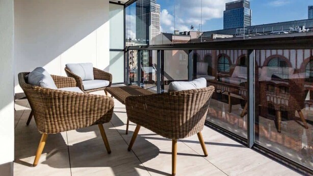 A balcony with wicker chairs and a glass wall offering a city view. - Modern Apartment with Air Conditioning | 2 Bedrooms | Parking (Warszawa)