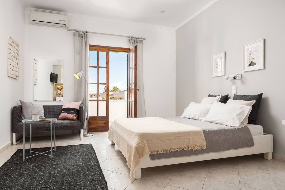 A bedroom with a bed, a bedside table, a chair, a window, and a door.
