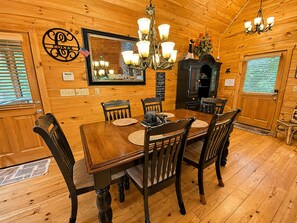 Un interior de madera con una mesa de comedor, sillas, una araña, una chimenea y un espejo.