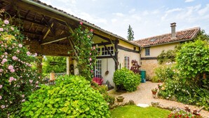 A traditional house with a garden, a covered porch, and a stone wall.