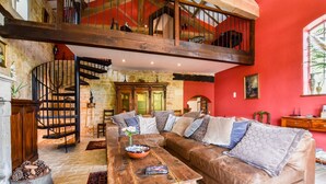 A spacious living room with a high ceiling, a wooden staircase, and a large sofa with multiple cushions.