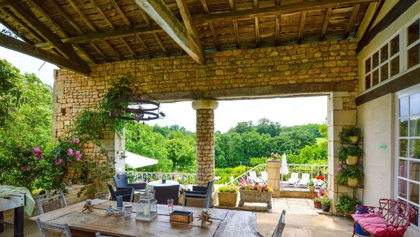 An outdoor patio with a stone wall, wooden table, and chairs.