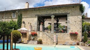A stone building with a pool, outdoor seating, and potted plants.
