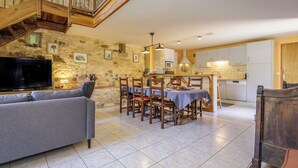 A spacious living area with a stone wall, a dining table set with chairs, a sofa, and a TV. - Casalle, comfortable restored holiday home with private swimming pool (Montcléra)