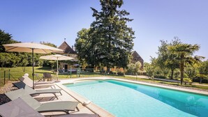 A swimming pool with lounge chairs and umbrellas, surrounded by a fence and trees. - Casalle, comfortable restored holiday home with private swimming pool (Montcléra)