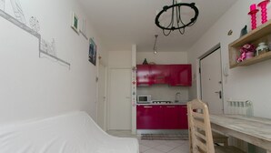 A bedroom with a bed, a wooden chair, a dining table, and a kitchen area with pink cabinets and a microwave. - M247 - Marcelli, new two-room apartment with terrace and garage (Marcelli)