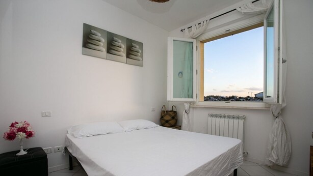 A bedroom with a bed, a window with curtains, a radiator, and a wall-mounted artwork. - M247 - Marcelli, new two-room apartment with terrace and garage (Marcelli)