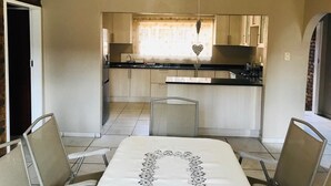 Een moderne keuken met een centraal eiland, een eethoek met een tafel en stoelen, en zicht op de keuken door een raam met een hartvormige decoratie.