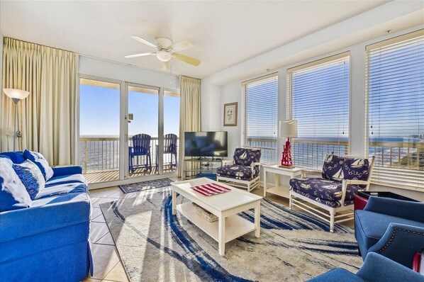 A spacious living room with a large TV, comfortable seating, and a view of the ocean. - Stunning West End View, Spring/Summer open, book your getaway now! (Panama City Beach)
