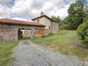 Une maison en pierre avec un toit en tuiles, une allée en gravier et une cour gazonnée.