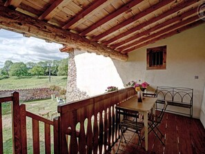 Une terrasse en bois avec un mur en pierre, une table avec des chaises et une fenêtre avec des barreaux.