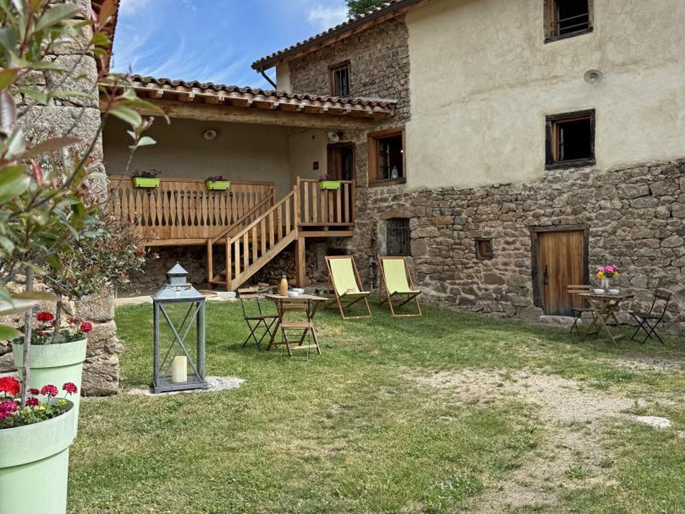 A rustic building with a stone wall, wooden balcony, and outdoor seating area with chairs and a table.