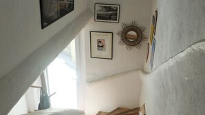 A staircase with wooden steps leading upwards, flanked by white walls. There are framed pictures and a sunburst mirror on the walls. - Charming village house in the Luberon (Cadenet)