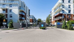 A modern apartment complex with a gated entrance, a blue directional sign, and a pedestrian pathway.