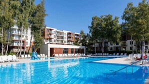 A swimming pool with lounge chairs and a water slide, surrounded by multi-story buildings with balconies.