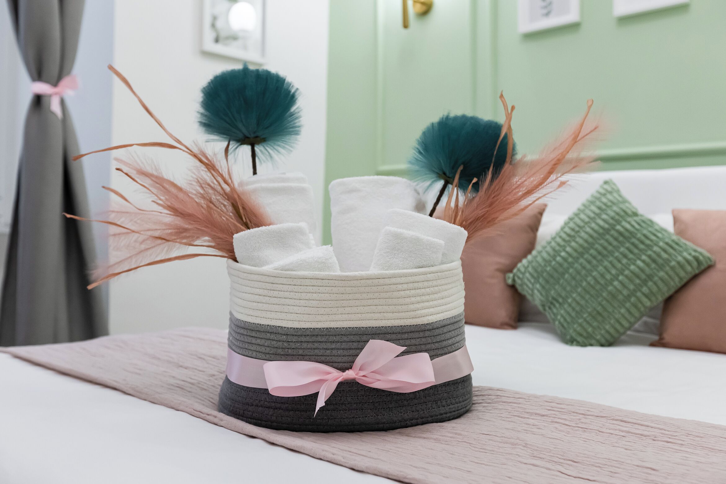 Un panier contenant des serviettes et des plumes décoratives, posé sur un lit.