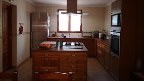 A kitchen with a central island, wooden cabinets, a refrigerator, a microwave, and a window with curtains. - The House of happiness (Alicante)