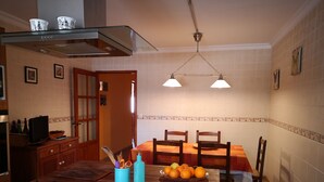 A kitchen with a gas stove, a dining table with chairs, a fruit bowl, and a blue container with utensils. - The House of happiness (Alicante)