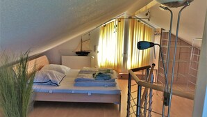 A bedroom with a bed, a radiator, a window with curtains, a plant, and a staircase.
