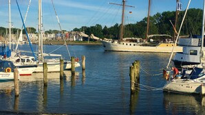 A marina with several sailboats docked, wooden pilings, and a building with flags in the background.
