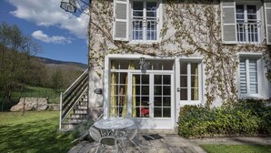 A stone staircase leading to a white door with a glass panel, a metal table and chairs outside, and a stone wall in the background. - Gite on the edge of the Arac in a green setting with swimming pool (Aleu)