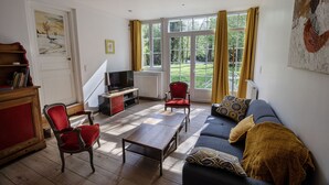 A living room with a sofa, two red chairs, a wooden coffee table, a television, and a bookshelf. - Gite on the edge of the Arac in a green setting with swimming pool (Aleu)