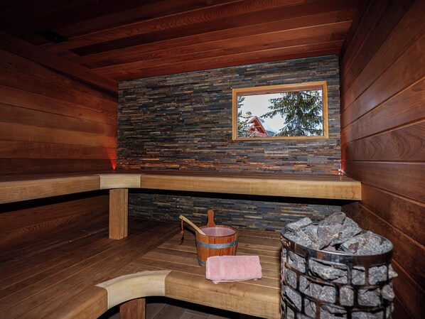 Ein Saunaraum mit Holzbänken, einer Steinwand und einem Fenster mit Bergblick.