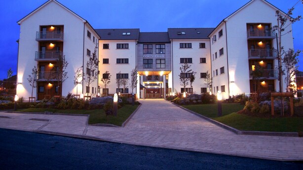 A multi-story hotel with a central entrance, balconies on each floor, and a well-maintained garden area. - Cuirt na Coiribe 4 bedroom Apartment (sleeps 5) (Galway)