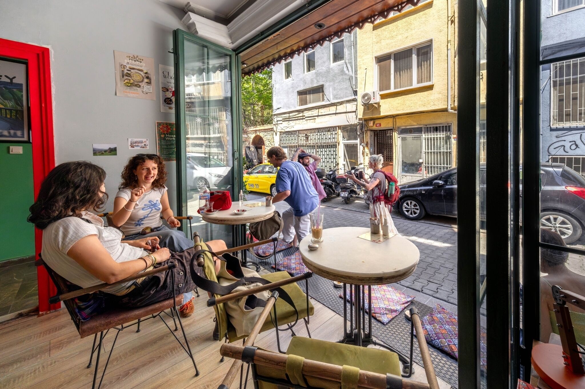 Um café ao ar livre com mesas e cadeiras, entrada por uma porta de vidro e vista para a rua.