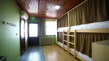 Una habitación con literas, techo de madera, radiador y una puerta con señal de salida.