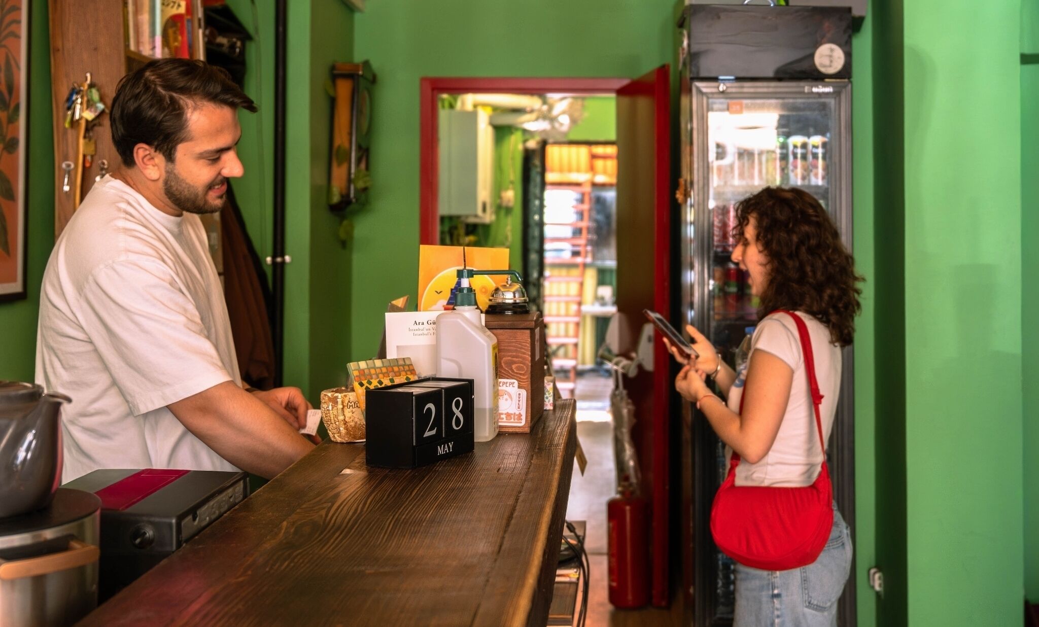 A bar with a wooden counter, a refrigerator, and a person using a smartphone.