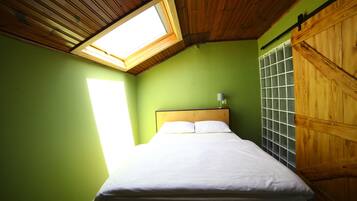 Un dormitorio con tragaluces, una cama con ropa blanca, cabecera de madera y pared verde.