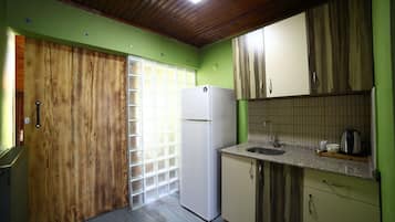 A compact kitchen with a wooden door, a white refrigerator, and a tiled backsplash.
