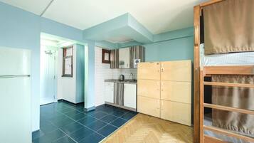 Quarto com cozinha compacta, piso de madeira e cama com cortina.