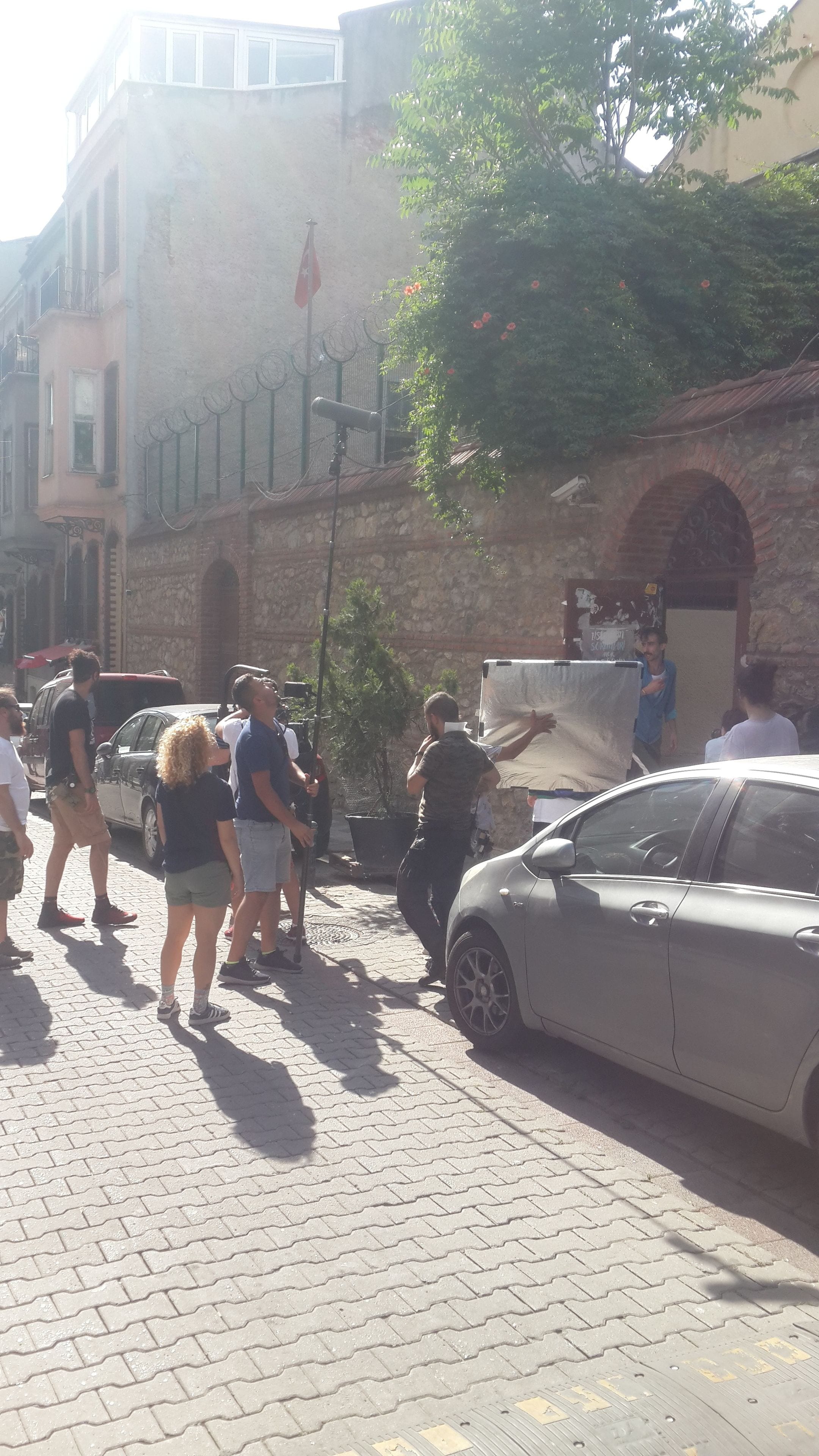 A cobblestone street with pedestrians and parked cars.