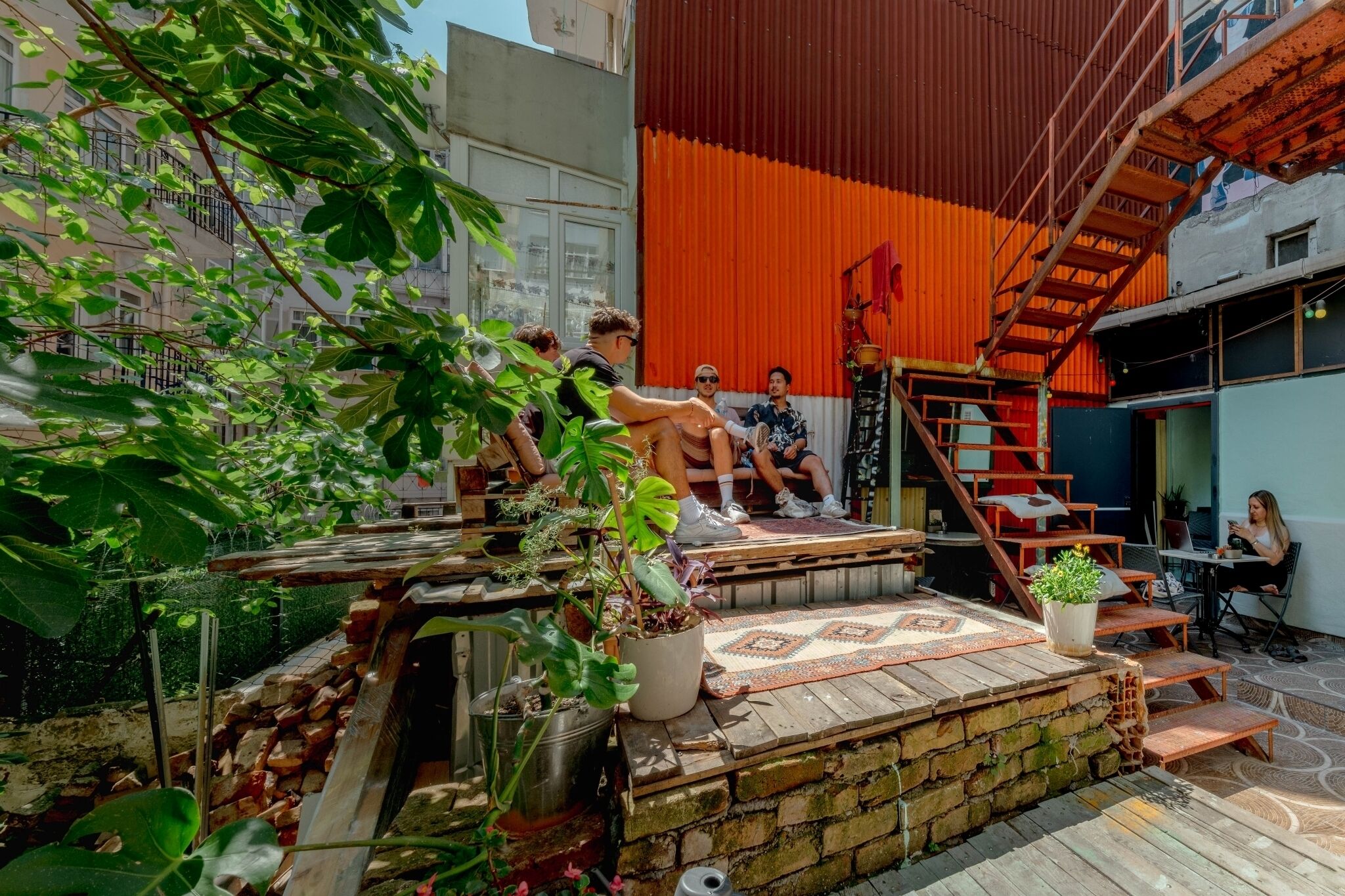 A rooftop terrace with a wooden deck, potted plants, and a staircase leading to an upper level.