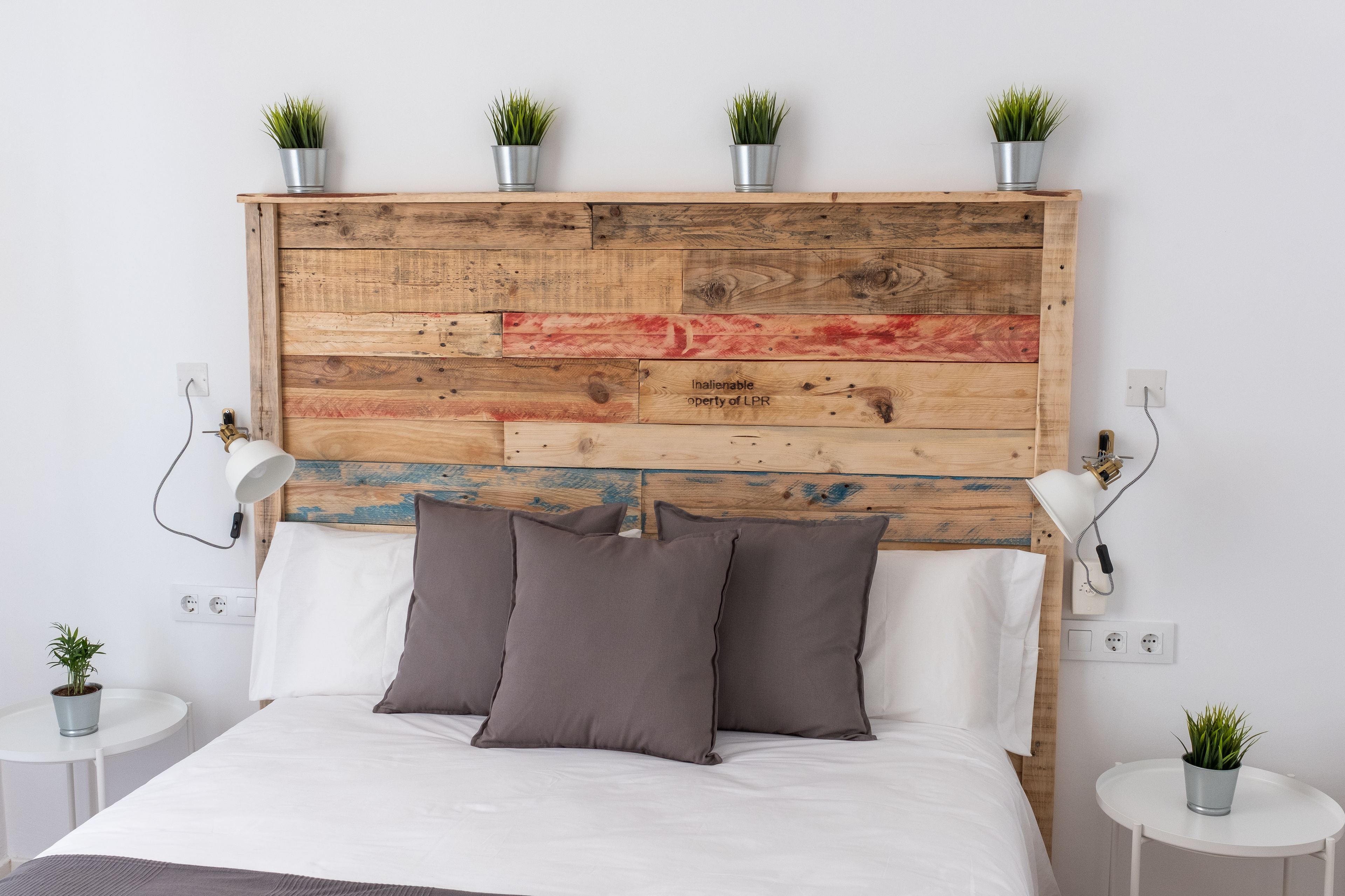 A bedroom with a wooden headboard, two bedside tables, a lamp, and a potted plant.