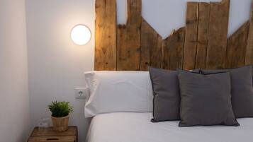 A bedroom with a wooden headboard, white bedding, and a bedside table with a plant and glasses.