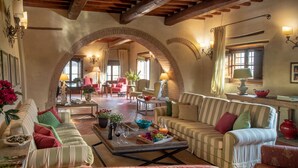 A spacious living area with a high ceiling, exposed wooden beams, and a brick archway leading to another room. There are multiple seating options including sofas and armchairs, and a coffee table with a fruit tray. - Beautiful private villa for 20 people with WIFI, private pool, sauna, TV and panoramic view (Rapale)