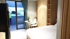 A hotel room with a bed, a desk, a chair, a wardrobe, and a sliding glass door leading to a balcony. - Tripporo - Homestay (Ho Chi Minh City)