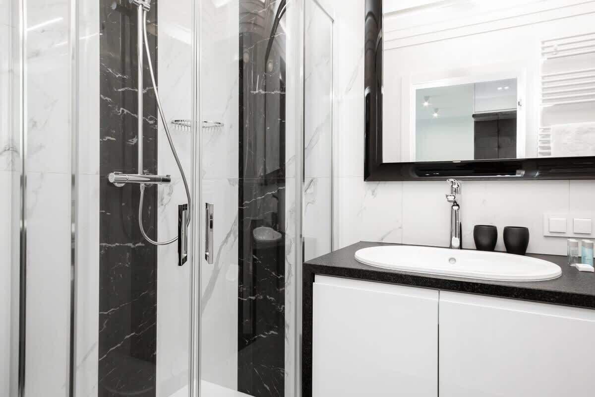 A modern bathroom with a glass-enclosed shower, a white sink, and a black countertop.