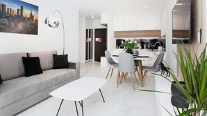 A modern living room with a sofa, a dining table with chairs, a flat-screen TV mounted on the wall, and a cityscape painting. - Air-conditioned Apartment with Balcony | Parking and Close to the Metro (Warszawa)