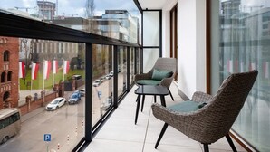 A balcony with wicker chairs and a table, overlooking a street with cars and buildings. - Air-conditioned Apartment with Balcony | Parking and Close to the Metro (Warszawa)