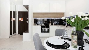 A modern kitchen with white cabinets, a built-in oven, and a dining area with a round table set for two. - Air-conditioned Apartment with Balcony | Parking and Close to the Metro (Warszawa)