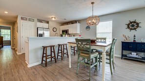 A kitchen with white cabinets, a central island, wooden stools, and a dining table with chairs.