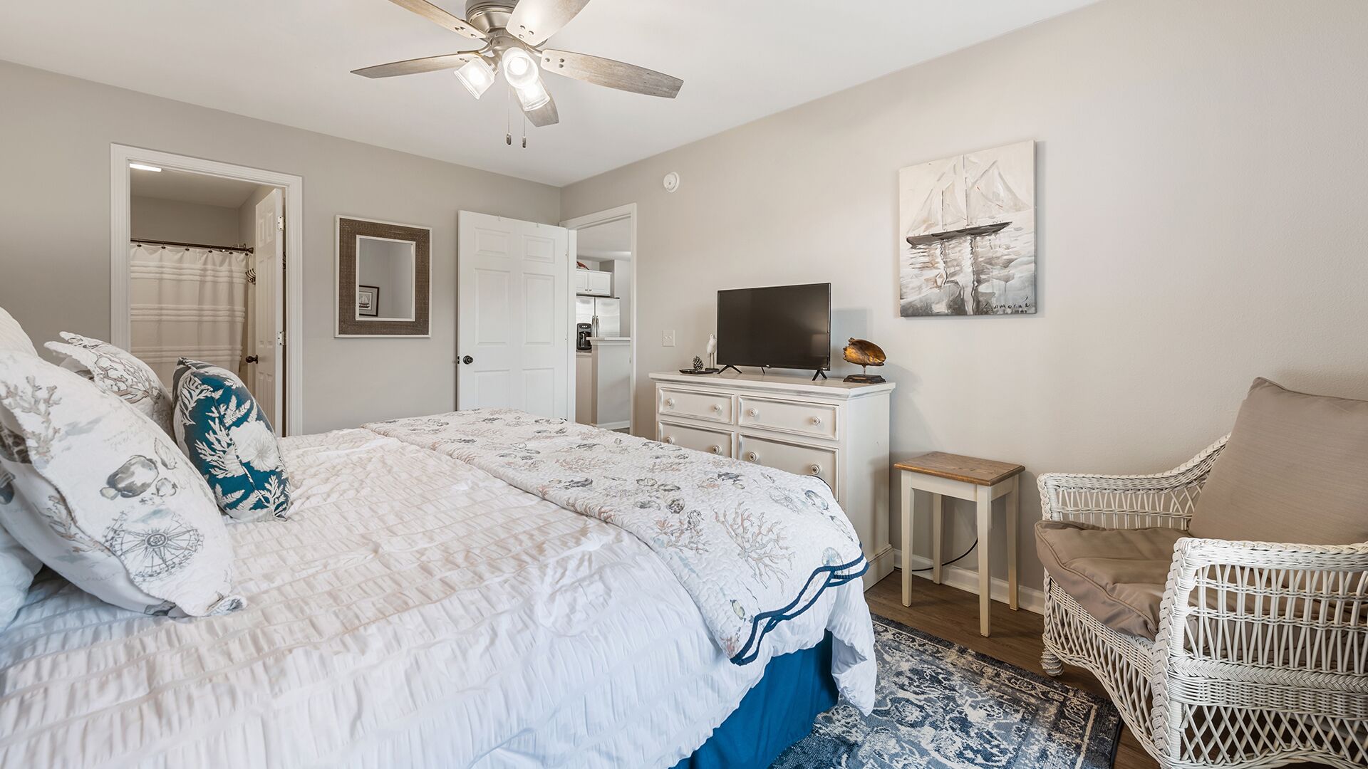 Une chambre à coucher avec un lit, un bureau, une chaise, un ventilateur de plafond et un tableau accroché au mur.