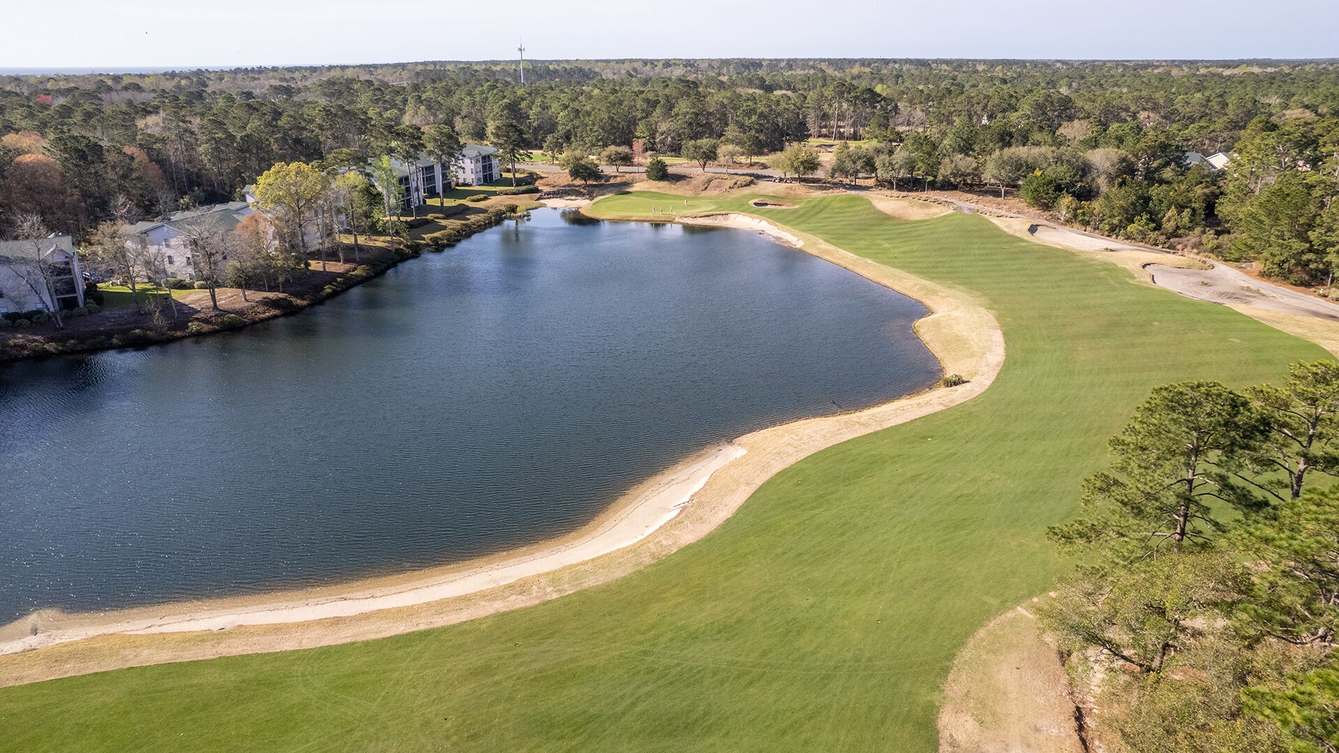 An aerial view of a golf course with a pond, surrounded by trees and buildings.