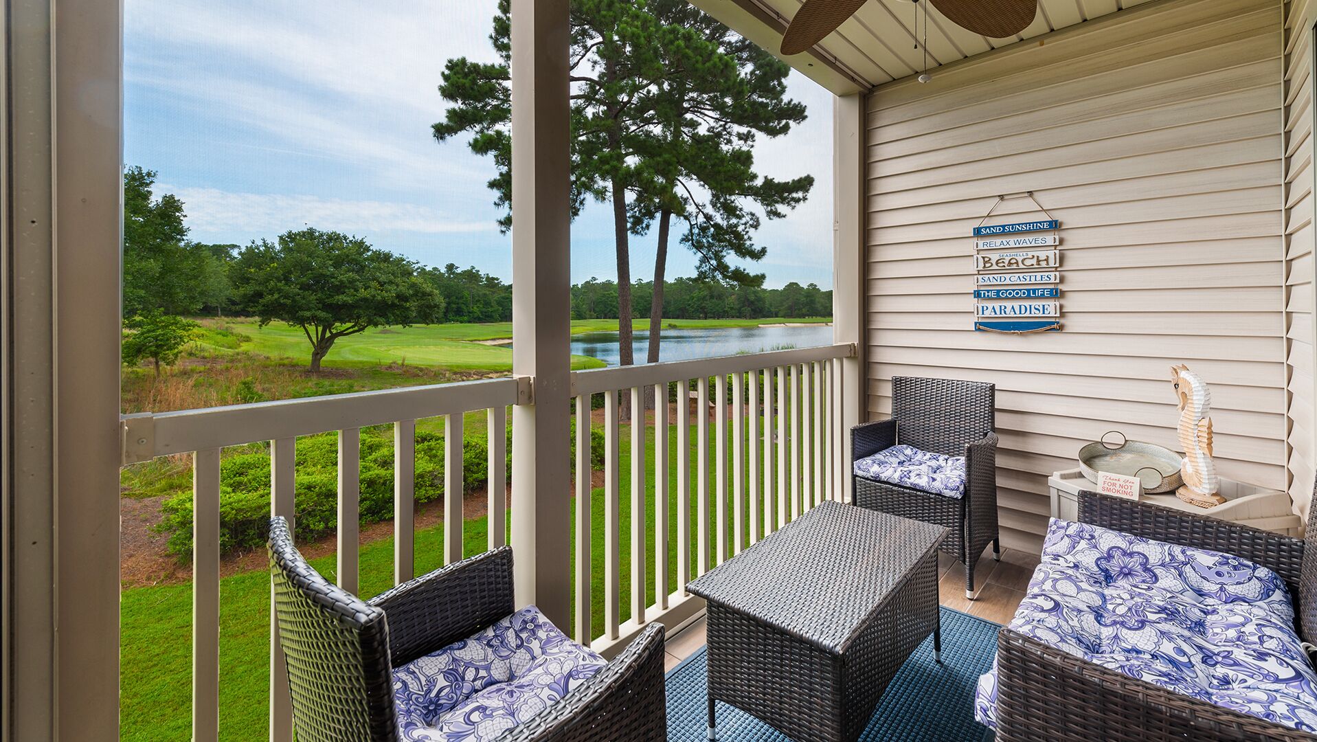 A porch with wicker furniture, a view of a golf course, and a sign with beach-related phrases.