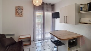 Cocina compacta con una mesa de comedor, horno integrado y televisor de pantalla plana montado en la pared.